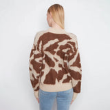 A woman viewed from behind wearing a fuzzy knit sweater with a brown and beige abstract pattern, paired with light blue jeans, against a plain white background.