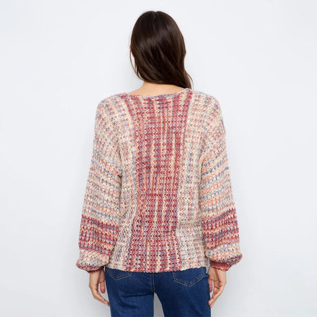 A woman viewed from behind wearing a chunky, multicolored knit sweater with blue jeans, set against a plain white studio background.