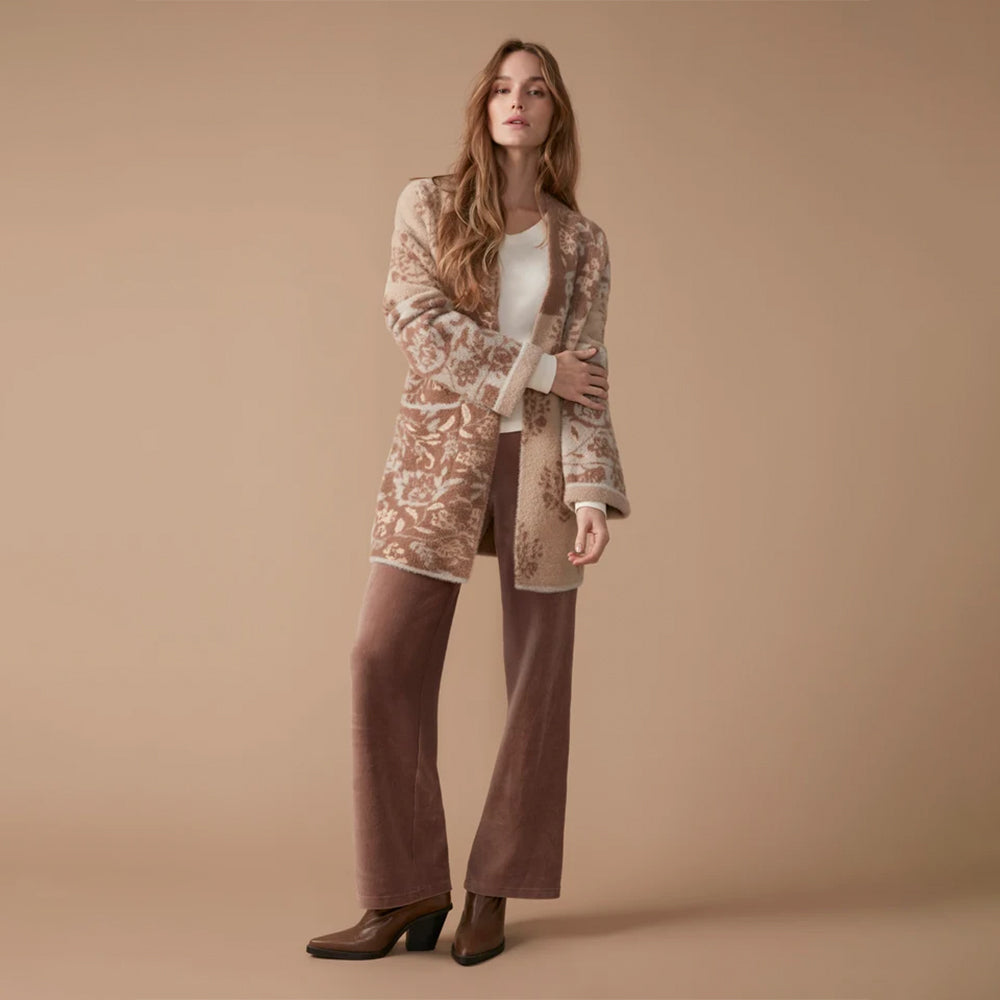 A woman models a mid-length open-front cardigan with an intricate beige and brown damask pattern, styled over a white top, brown wide-leg pants, and brown ankle boots against a solid beige studio backdrop.