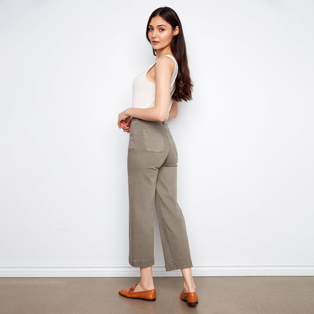 Woman wearing a white top and green pants against a plain white background