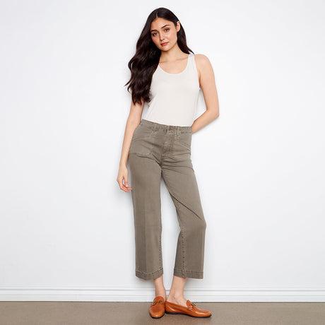 Woman wearing a white tank top and green pants against a white background