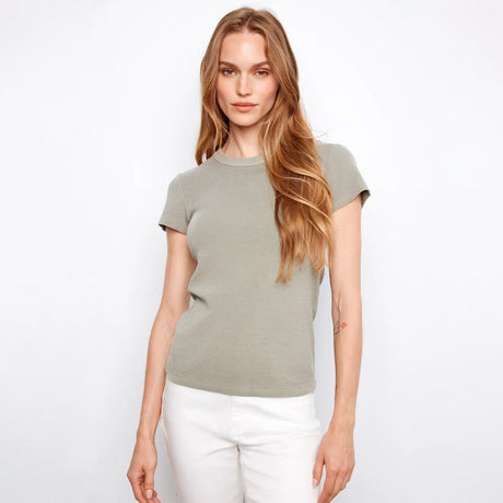 Woman wearing a green t-shirt and white pants on a light gray background
