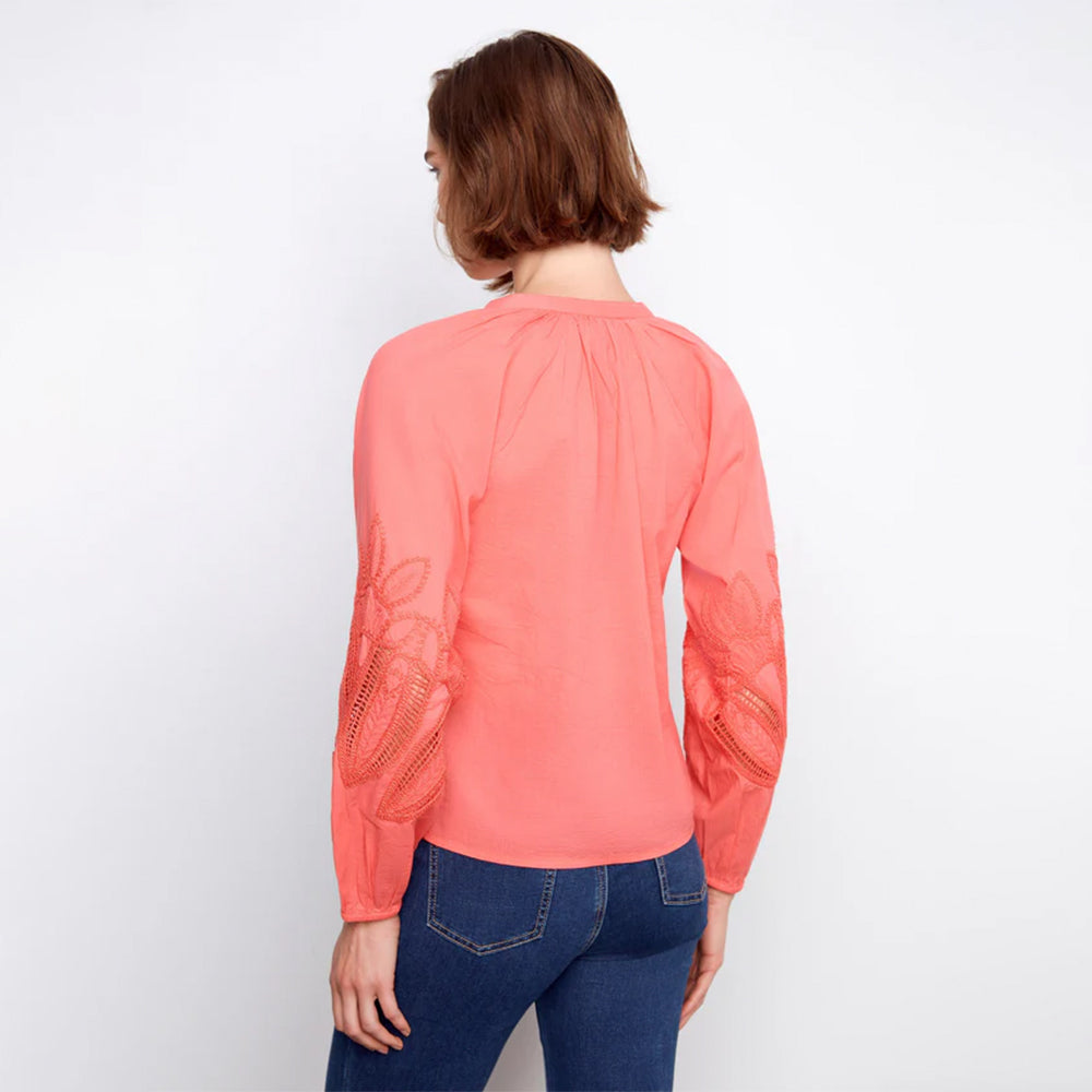 Person wearing a coral long-sleeve top with lace details on a white background