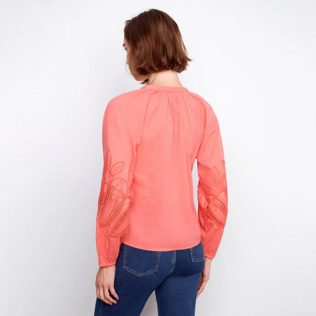 Person wearing a coral long-sleeve top with lace details on a white background