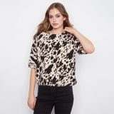 A woman modeling a short-sleeve crewneck top with a black and beige cow-print pattern, paired with black jeans, against a plain white studio background.