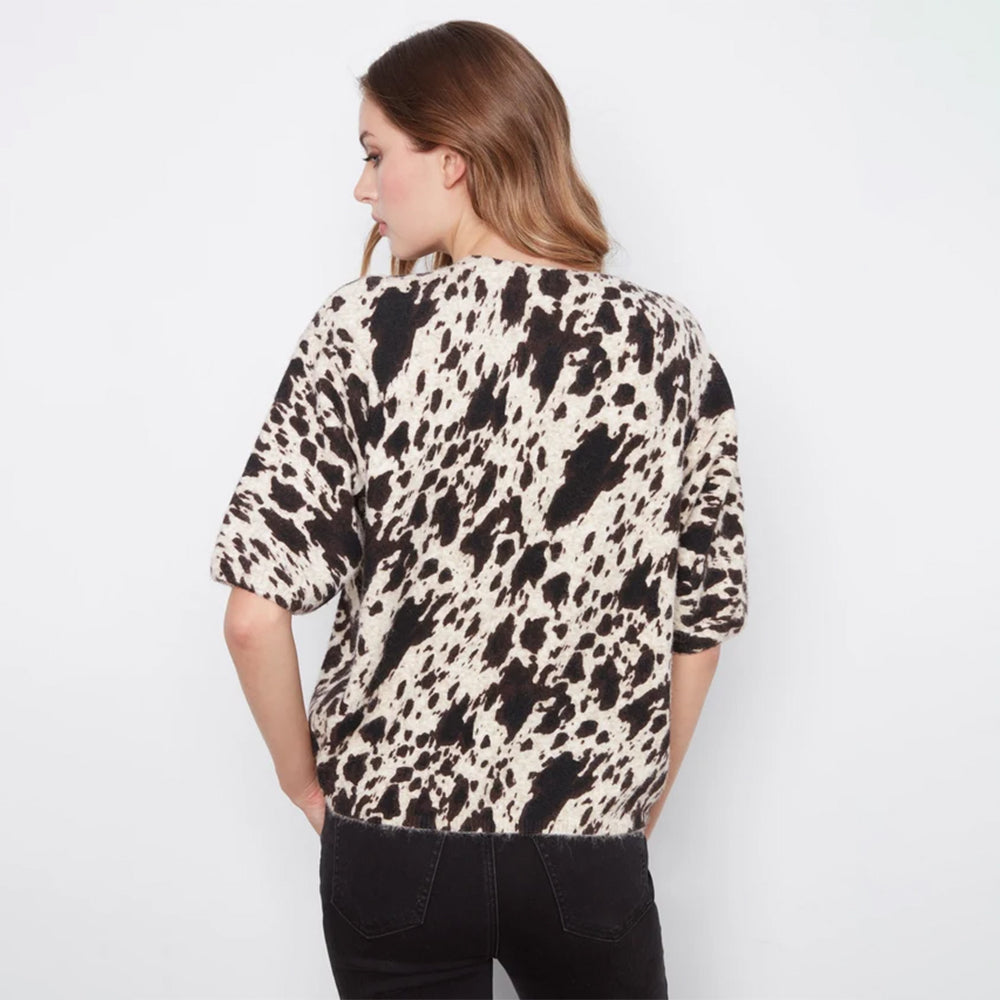 A woman shown from the back wearing a short-sleeve top with a black and cream cow-print pattern, paired with black jeans, against a plain white background.