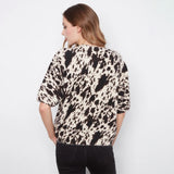 A woman shown from the back wearing a short-sleeve top with a black and cream cow-print pattern, paired with black jeans, against a plain white background.