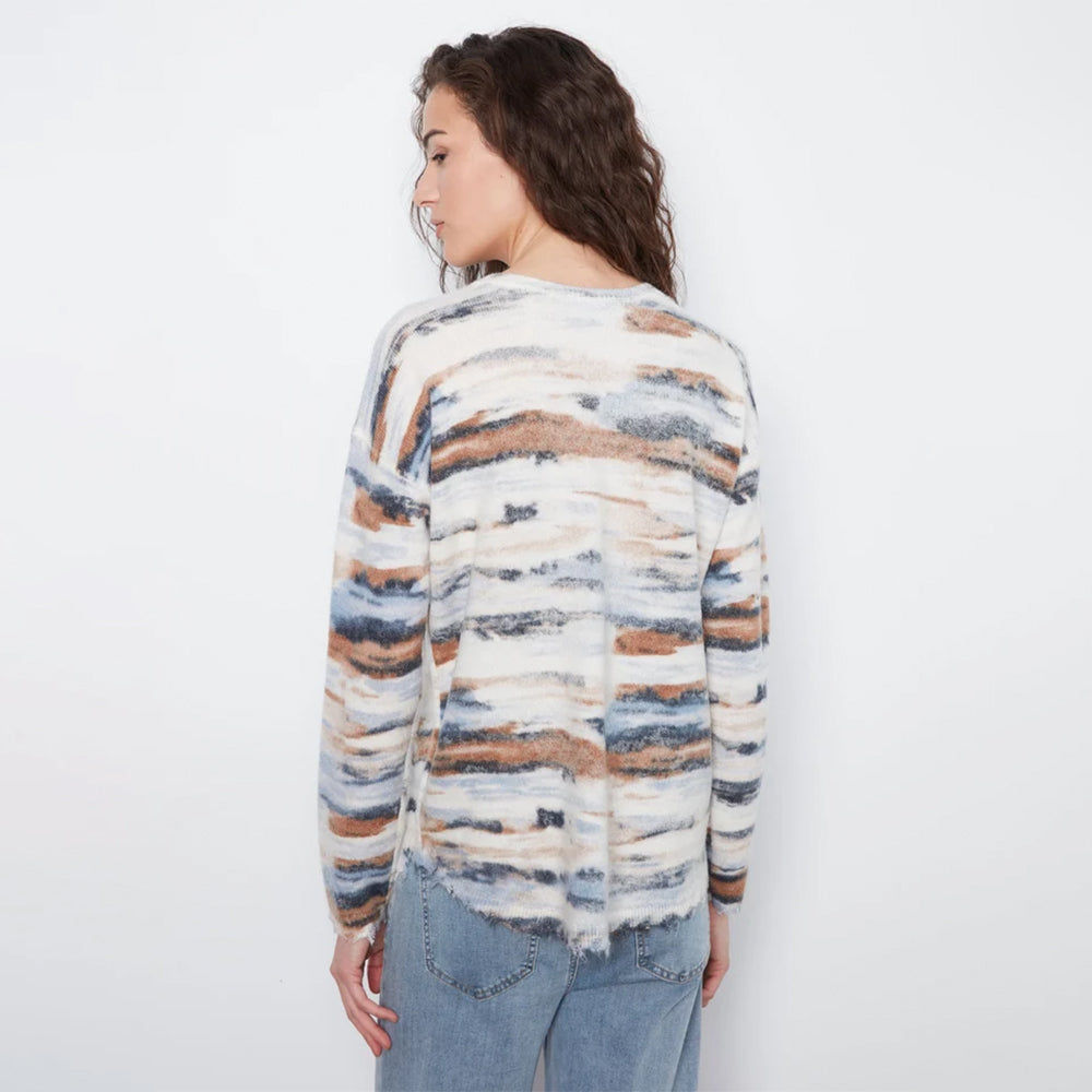 A woman shown from the back wearing a fuzzy knit sweater with horizontal watercolor-style stripes in cream, brown, blue, and gray, paired with light blue jeans against a plain white background.