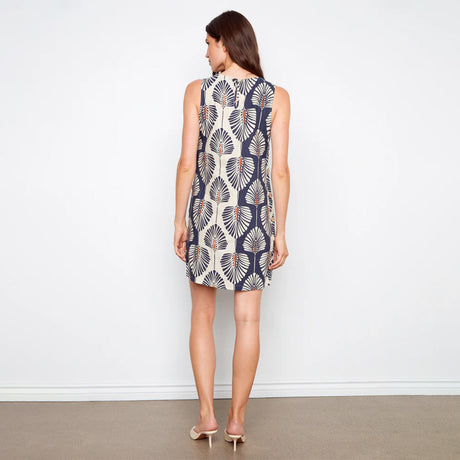 Woman wearing a sleeveless dress with a leaf pattern against a plain background