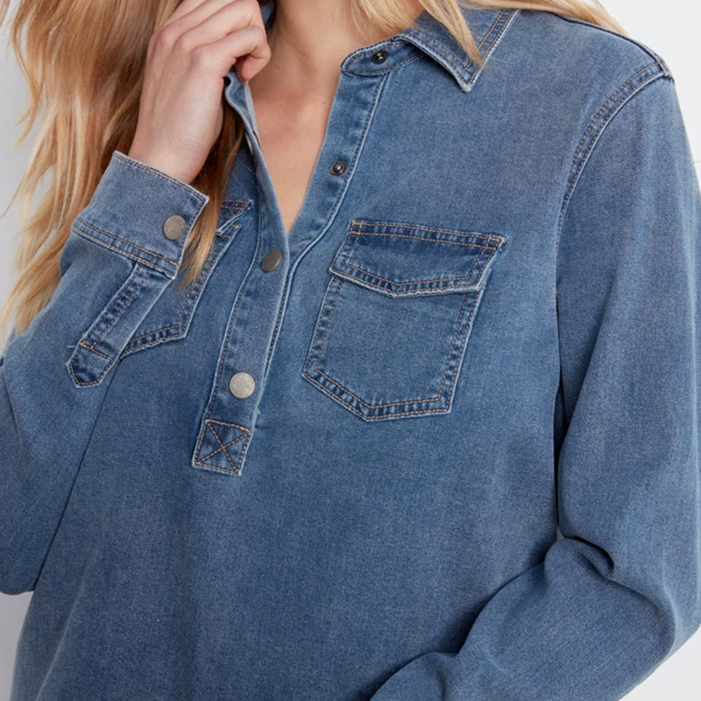 A close-up of a person wearing a blue denim long-sleeve button-up shirt with chest pockets and metal buttons.