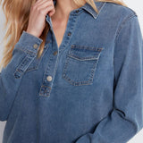 A close-up of a person wearing a blue denim long-sleeve button-up shirt with chest pockets and metal buttons.
