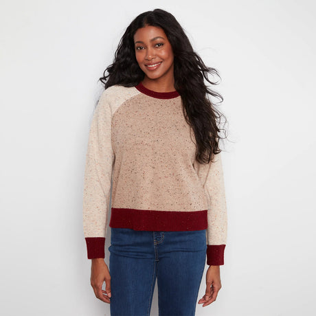 A woman modeling a crewneck sweater with a speckled beige body, contrasting burgundy collar, hem, and cuffs, paired with blue jeans against a plain white background.