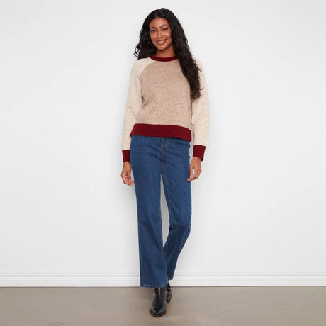 A woman modeling a cream and burgundy knit sweater with blue wide-leg jeans and black boots, standing against a plain white wall.