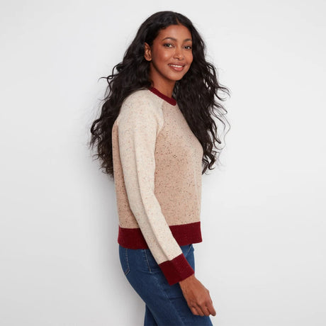 A woman modeling a cream-colored knit sweater with burgundy ribbed collar, cuffs, and hem, paired with blue jeans against a plain white background.