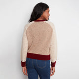 A woman shown from the back wearing a color-blocked knit sweater with a speckled beige body, burgundy collar, hem, and cuffs, paired with blue jeans against a plain white background.