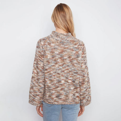 A woman viewed from the back wearing a chunky knit mock-neck sweater with a marled pattern of brown, beige, and cream, paired with light blue jeans against a plain white background.