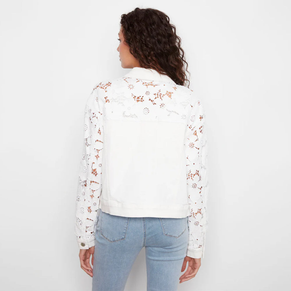 Woman wearing a white floral lace top and light blue jeans on a plain background