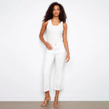 Woman wearing a white sleeveless top and pants against a plain background