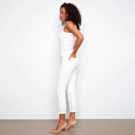 Woman wearing a white sleeveless top and pants against a plain background