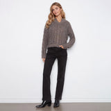 A woman stands against a plain white wall wearing a fuzzy taupe-brown cropped sweater, black pants, and black ankle boots.