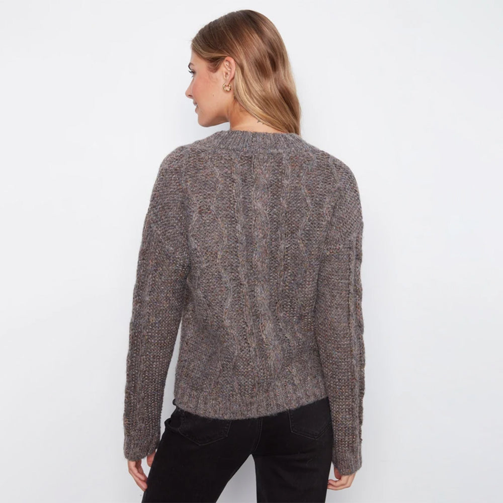 A woman viewed from the back wearing a textured, cable-knit crewneck sweater in a heathered brown and gray color, paired with black pants, against a plain white background.
