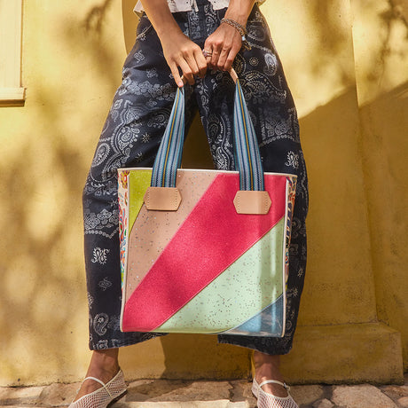 Person holding a colorful tote bag against a yellow wall