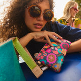 Woman holding a colorful floral-patterned wallet with another person in the background.