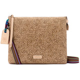 A tan embossed leather crossbody bag with a floral paisley pattern, featuring a colorful woven strap and a leather hangtag on a white background.