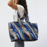 Person holding a large blue and brown marbled tote bag against a white background