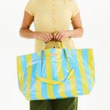Person holding a yellow and blue striped bag with a visible brand logo.
