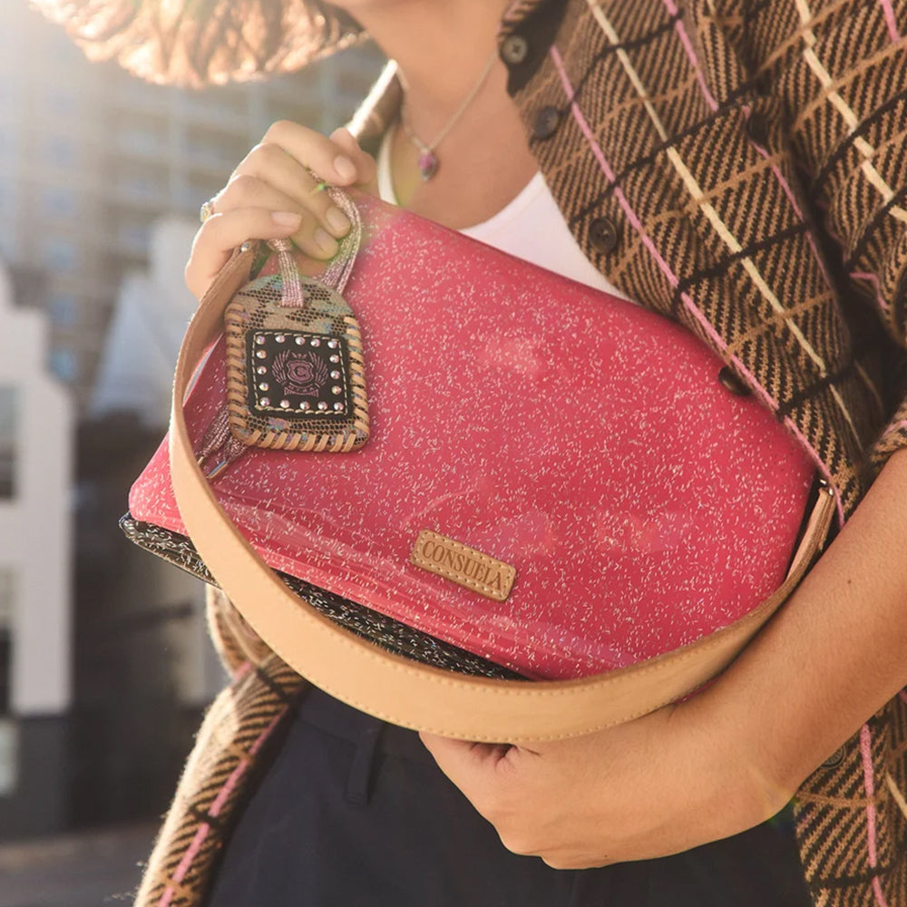 A person holding a pink glittery clutch bag with a tan leather strap and a decorative hanging charm. The bag has a small gold-tone 'CANADA' logo plaque.