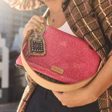 A person holding a pink glittery clutch bag with a tan leather strap and a decorative hanging charm. The bag has a small gold-tone 'CANADA' logo plaque.