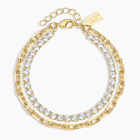 A gold-toned layered chain bracelet with clear cubic zirconia stones, shown on a light gray background. The brand name 'LUXORING' is engraved on a small tag attached to the clasp.
