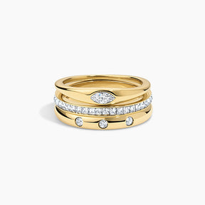 A stack of three gold rings on a light gray background. The top ring is plain gold, the middle ring is paved with clear stones, and the bottom ring is gold with three small clear stones spaced along it.