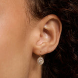 A close-up of a person's ear wearing a small gold dangle earring with a circular cluster of clear stones.