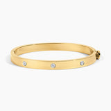 A polished yellow gold bangle bracelet with three small round clear gemstones spaced along the front, shown on a clean white background.