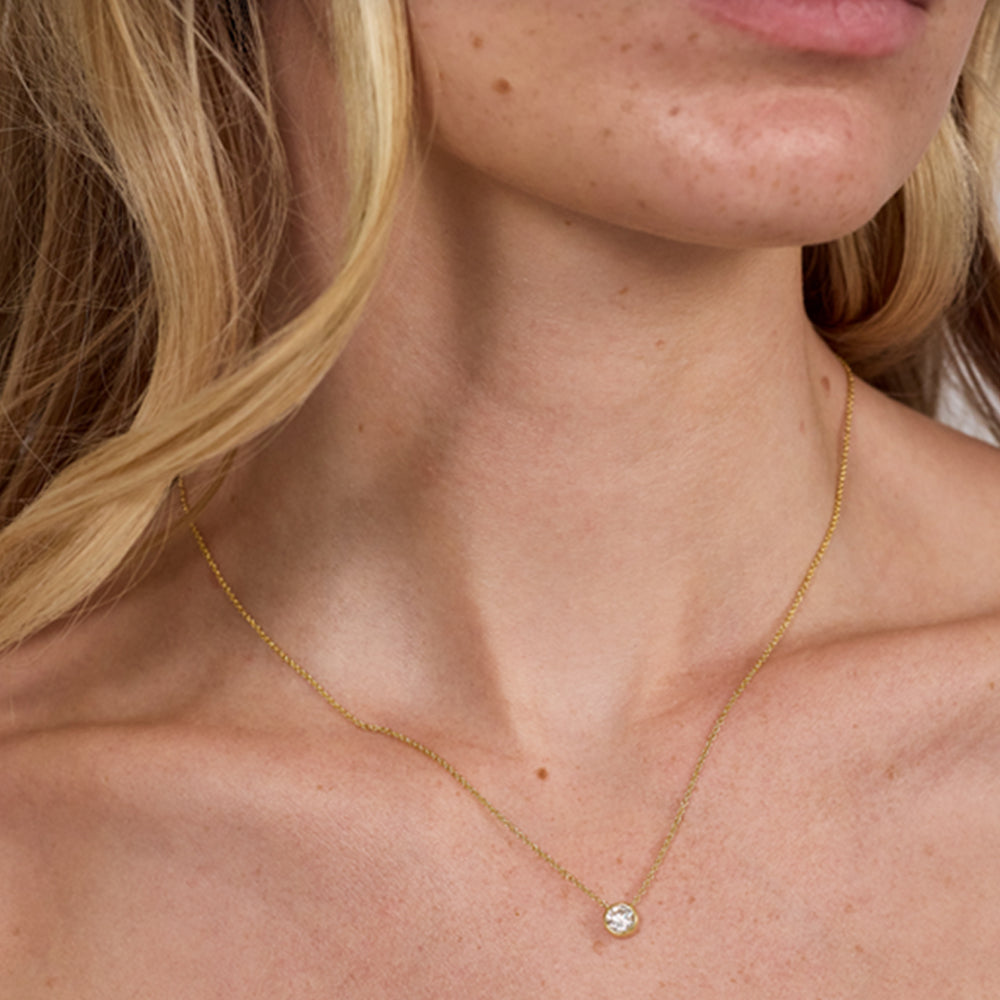Close-up of a woman wearing a gold necklace with a small diamond pendant.