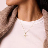 Gold necklace with a cross pendant worn by a person in a white shirt and brown coat.