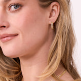 Close-up of a woman wearing gold hoop earrings with a neutral background