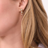 Close-up of a person wearing gold earrings with clear gemstones.