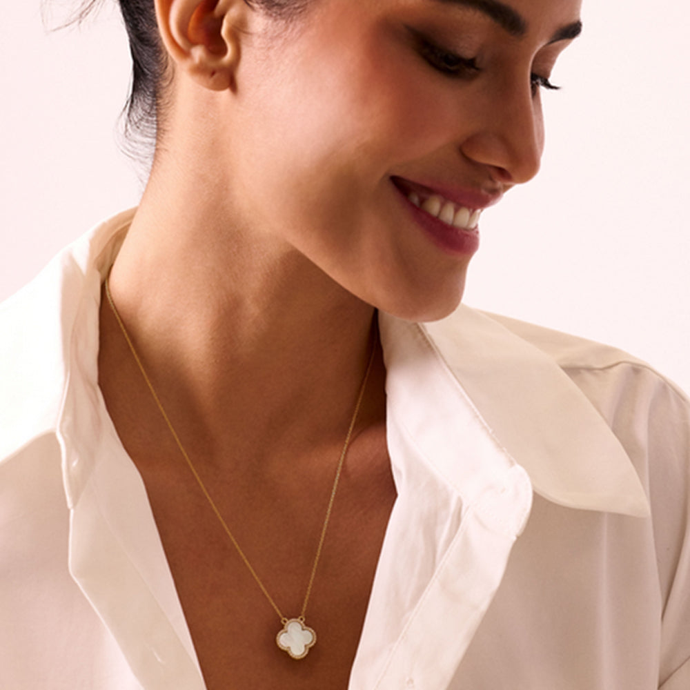 Woman wearing a gold necklace with a white pendant on a plain background