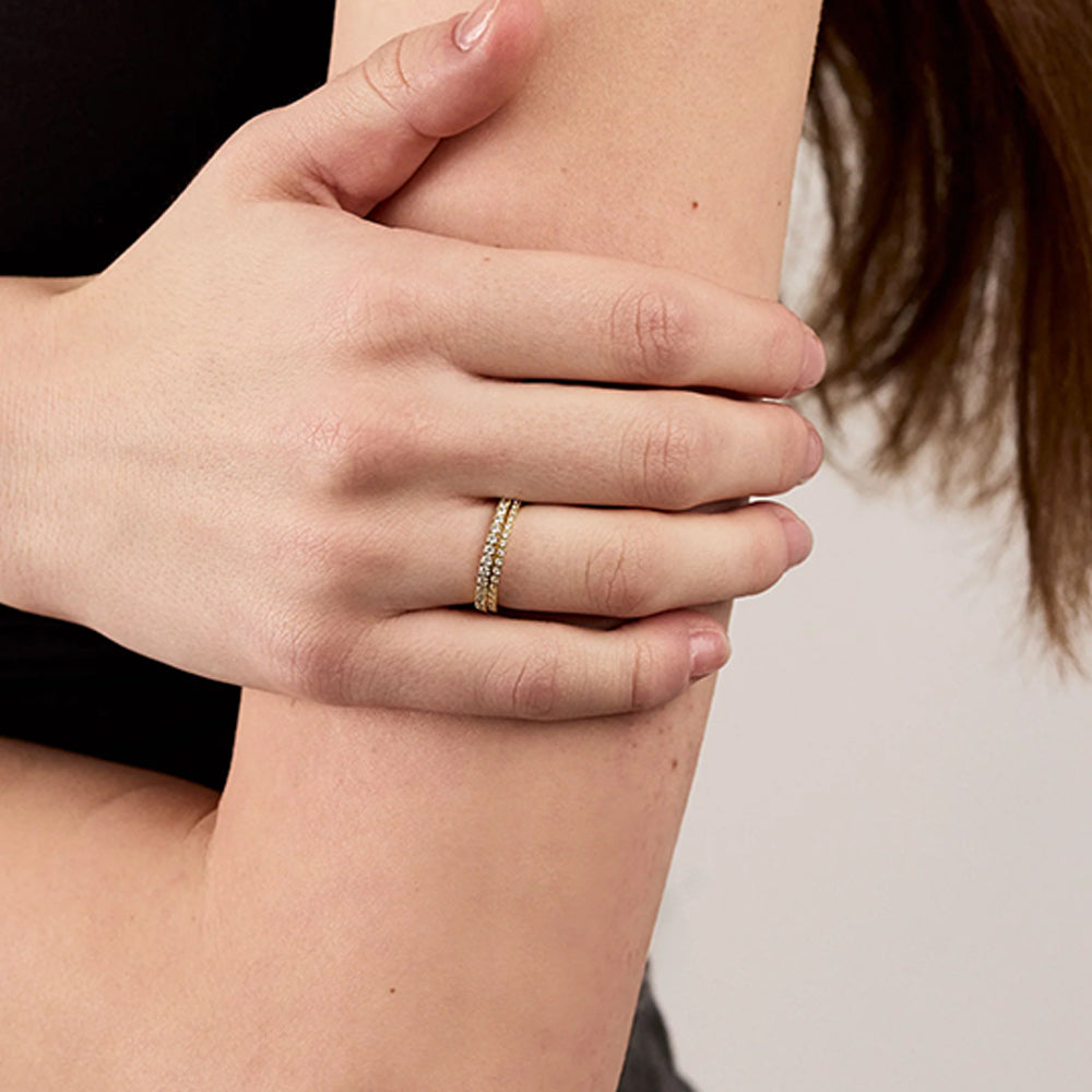 A close-up of a person's hand resting on their arm, wearing a delicate gold band ring with small clear stones on the ring finger.