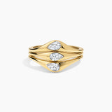 A gold ring with three stacked, wavy bands featuring pear-cut clear gemstones, set against a clean white background.