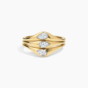 A gold ring with three stacked, wavy bands featuring pear-cut clear gemstones, set against a clean white background.