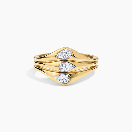 A gold ring with three stacked, wavy bands featuring pear-cut clear gemstones, set against a clean white background.