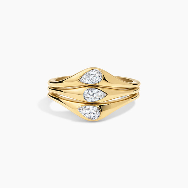 A gold ring with three stacked, wavy bands featuring pear-cut clear gemstones, set against a clean white background.