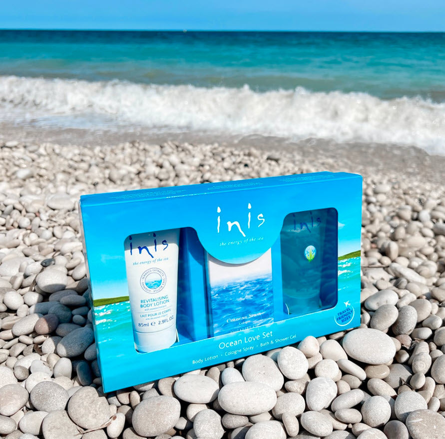 Beach in the background with a box of Inis bath and body lotion & perfumes sitting on a bed of rocks