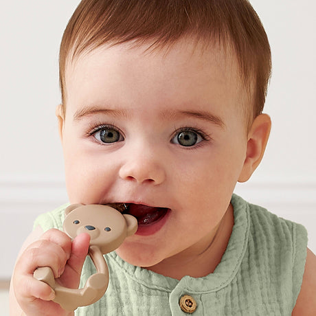 Baby holding a teething toy with a plain background