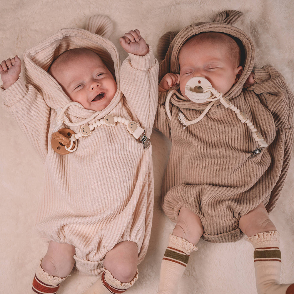 Two babies in matching ribbed rompers and hats on a soft surface.