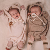 Two babies in matching ribbed rompers and hats on a soft surface.